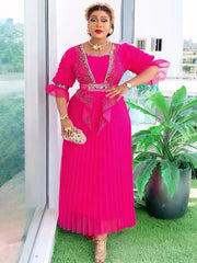 A woman wears a vibrant pink pleated maxi dress with embellished bodice details and sheer sleeves.