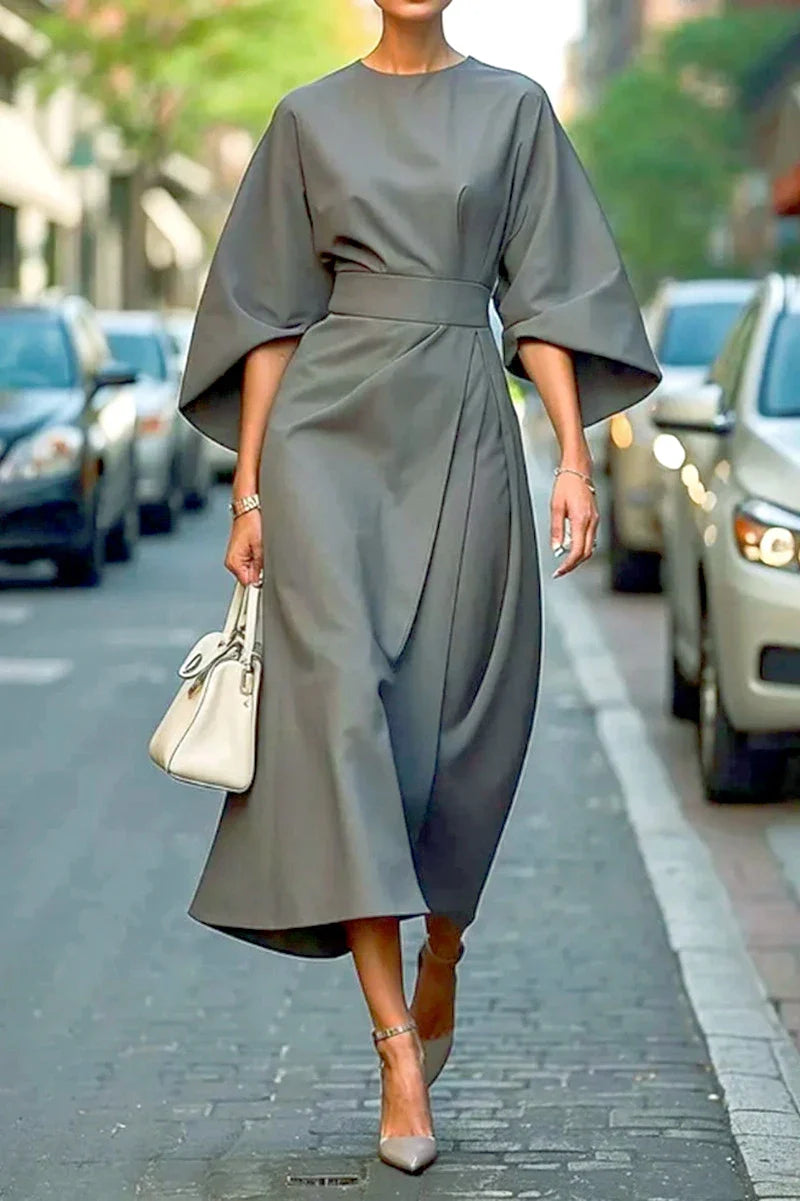 A woman wears an elegant grey ankle-length dress with bat sleeves and a fitted waist.