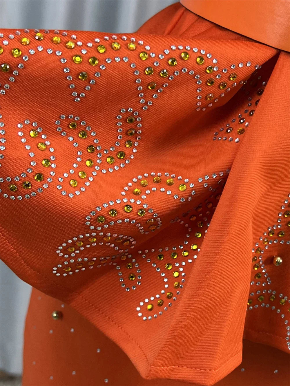 An orange ankle-length dress featuring geometric patterns embellished with yellow and clear crystals.