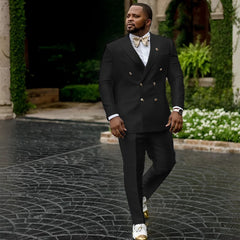 A man wears a black double-breasted suit with a white shirt and a gold bow tie.