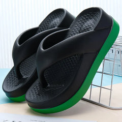 A pair of black platform flip-flops with a green sole and textured footbed.