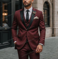 A man wears a three-piece burgundy suit with a black shawl collar, white shirt, and black tie.