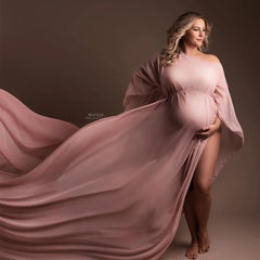A pregnant woman wears a flowing, dusty pink chiffon maternity cape with a boat neckline.