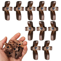 A hand holds several small wooden pocket crosses, each featuring a carved heart in the center.