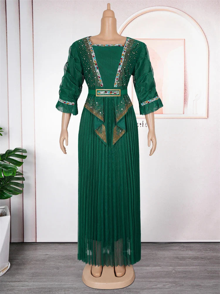 A floor-length emerald green pleated dress with embellished trim and a matching waist belt.