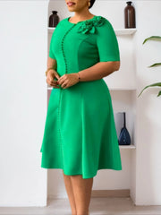 A woman wears a knee-length green A-line dress with short sleeves, button details, and floral trim.