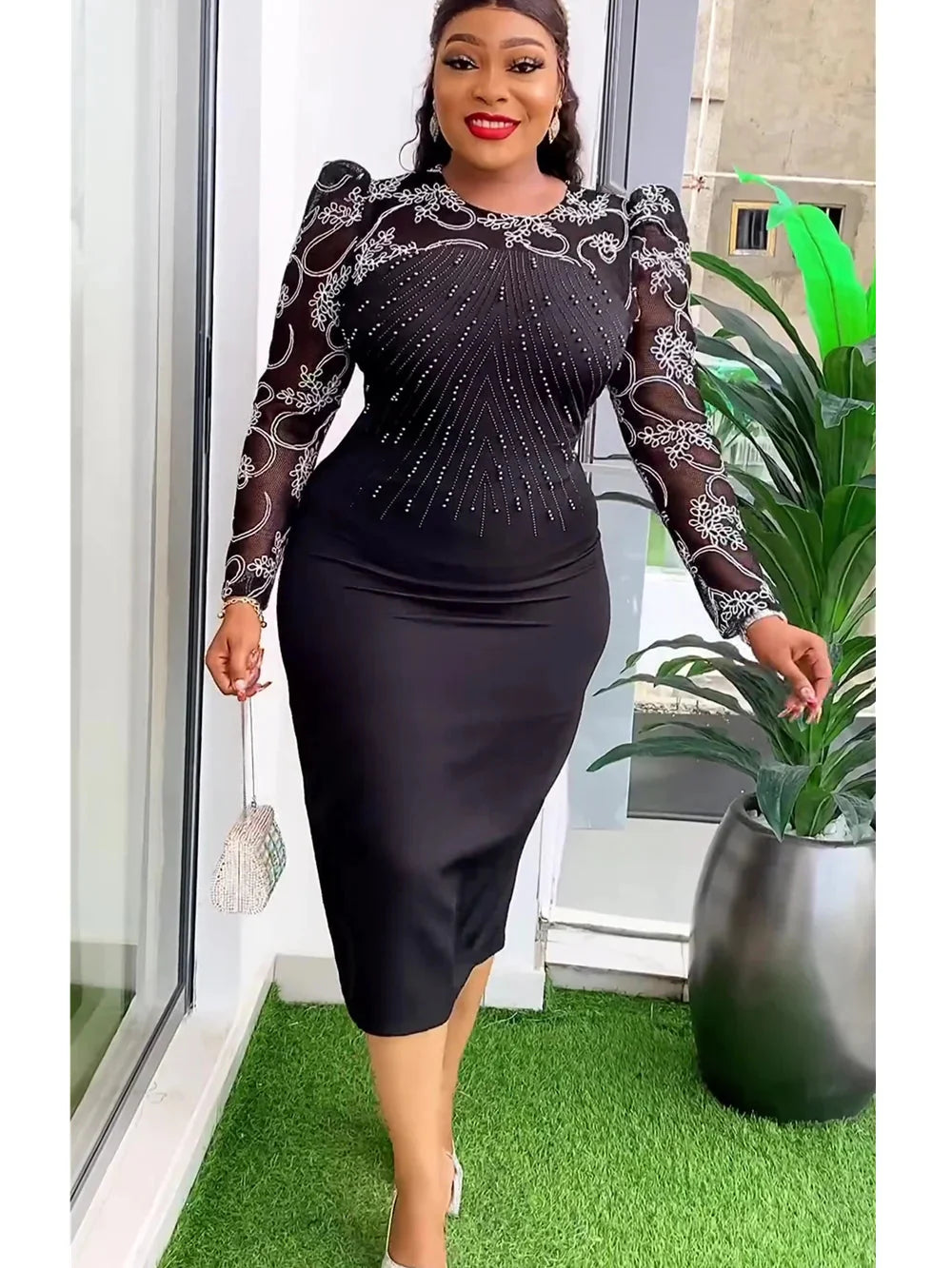 A woman wears a black midi dress with sheer long sleeves featuring white floral embroidery.