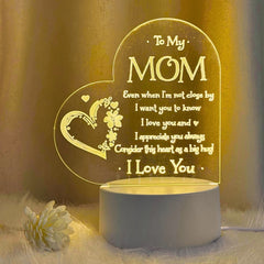 A heart-shaped acrylic night light for mom with engraved text and floral designs on a round base.