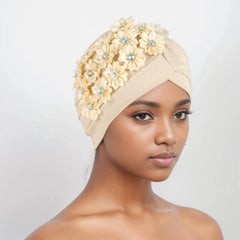A beige pleated turban headscarf decorated with fabric flowers and rhinestones.