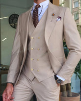 A man wears a beige three-piece suit with a double-breasted vest, peak lapels, and a patterned tie.