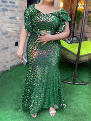 A woman wears a floor-length, emerald green sequined mermaid dress with petal sleeves.