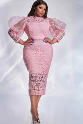 A woman wears a pink lace midi dress with sheer puff sleeves and a slim sheath silhouette.