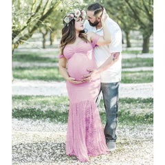 A pregnant woman wears a pink off-the-shoulder lace mermaid maternity dress for a photo shoot.