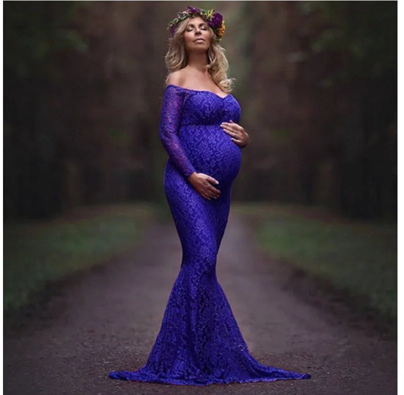 A pregnant woman wears a long-sleeved, off-shoulder royal blue lace mermaid maternity gown.