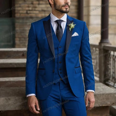 A man wears a royal blue three-piece suit with a black shawl collar, white shirt, and black tie.