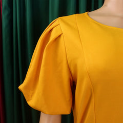 A close-up of a mustard yellow dress featuring a round neckline and pleated puff sleeves.