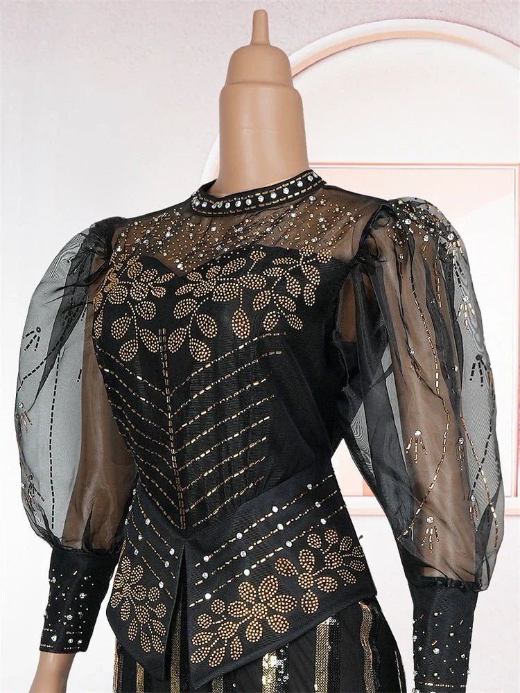 A black floor-length evening gown with gold sequin floral patterns and sheer puff sleeves.