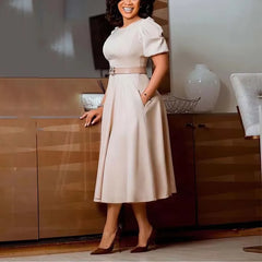 A woman wears a beige short-sleeved midi dress with a belted waist and pleated A-line skirt.
