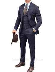A man wears a dark blue three-piece suit with a peak lapel, white shirt, and brown tie.