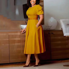 A woman wears a mustard yellow midi dress with short sleeves, a belted waist, and side pockets.
