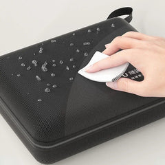 A hand wipes water droplets off the surface of a black, rectangular, zippered storage case.
