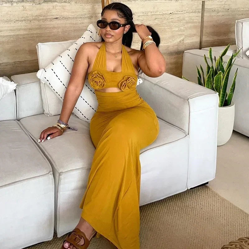 A woman wears a mustard yellow ankle-length halter dress featuring floral accents on the bodice.