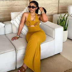 A woman wears a mustard yellow ankle-length halter dress featuring floral accents on the bodice.
