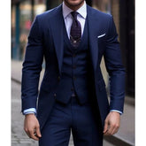 A man wears a slim-fit navy blue three-piece suit with a notched lapel and a textured tie.