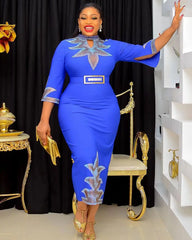 A woman wears a royal blue midi dress with silver leaf-patterned accents and a matching belt.