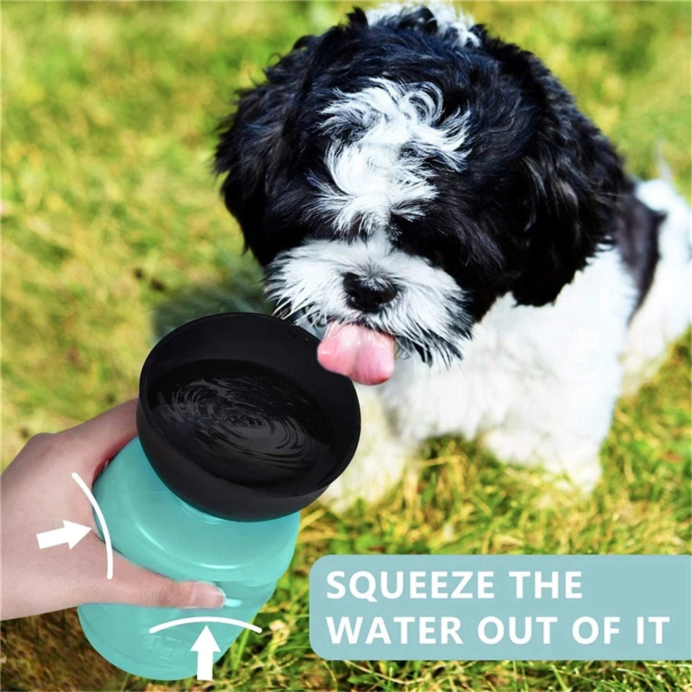 A person squeezes a teal portable dog water bottle with a black bowl top as a puppy drinks.
