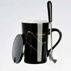 A black ceramic mug featuring a gold Gemini constellation design with a matching lid and spoon.
