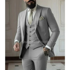 A man wears a slim-fit light gray three-piece suit with a matching vest and a light tie.
