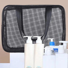 A black rectangular mesh tote bag sits behind several white pump bottles of toiletries.