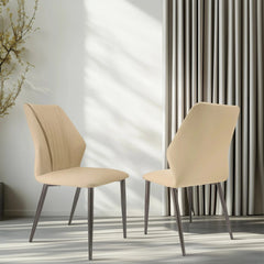 Two beige upholstered PU leather dining chairs with dark metal legs stand in a bright room.