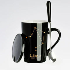 A black ceramic mug featuring a gold Libra constellation design, complete with a lid and spoon.