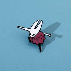 A metal enamel pin of the character Hornet from Hollow Knight on a blue background.