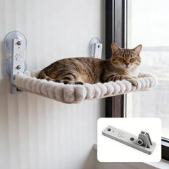 A brown tabby cat rests on a plush, cream-colored window hammock mounted with suction cups.