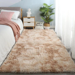 A rectangular, plush, beige-toned shaggy rug placed on a bedroom floor next to a bed.