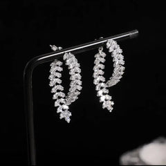 A pair of silver-toned stud earrings featuring a curved leaf design encrusted with clear zircons.