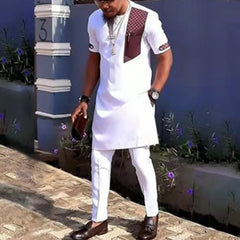 A man wearing a white two-piece African-style suit with a patterned chest pocket and sleeve detail.