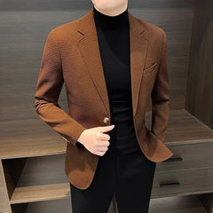 A man wears a brown textured single-breasted blazer over a black turtleneck and black trousers.