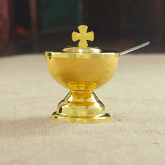 A small golden communion cup with a cross-topped lid and a matching spoon.
