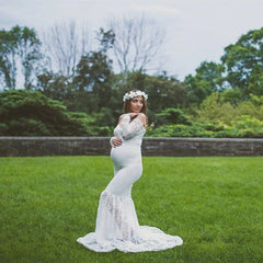 A pregnant woman wears a white off-shoulder lace mermaid maternity gown in a grassy field.