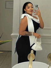 A woman wears a sleeveless black mid-length dress featuring a white bow detail on the shoulder.