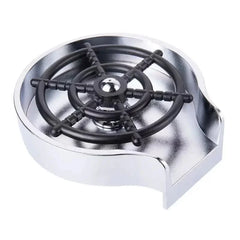 An automatic glass cup rinser with a black ship wheel design set in a silver metal base.