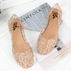 A pair of gold glittery, hollow-patterned jelly sandals with a flat sole.