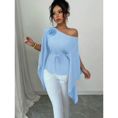 A woman wears a light blue, slash-neck long-sleeve shirt with a floral accent and waist tie.