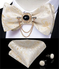 A pink paisley bow tie set featuring a decorative brooch with a black stone and gold chains.