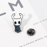 A Hollow Knight enamel pin featuring the character with a blue cloak and a metal backing clutch.