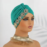 A teal pleated turban headscarf decorated with a row of circular rhinestone embellishments.